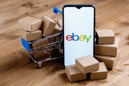 eBay logo on phone with shopping trolley and parcels
