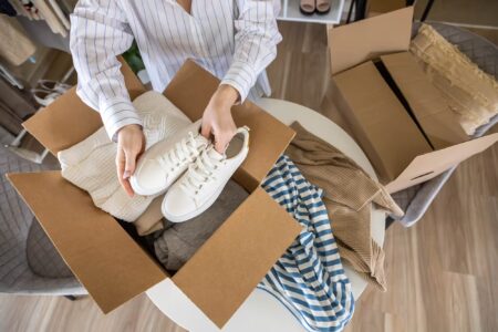 packing clothes and shoes into cardboard box for donation charity online shopping